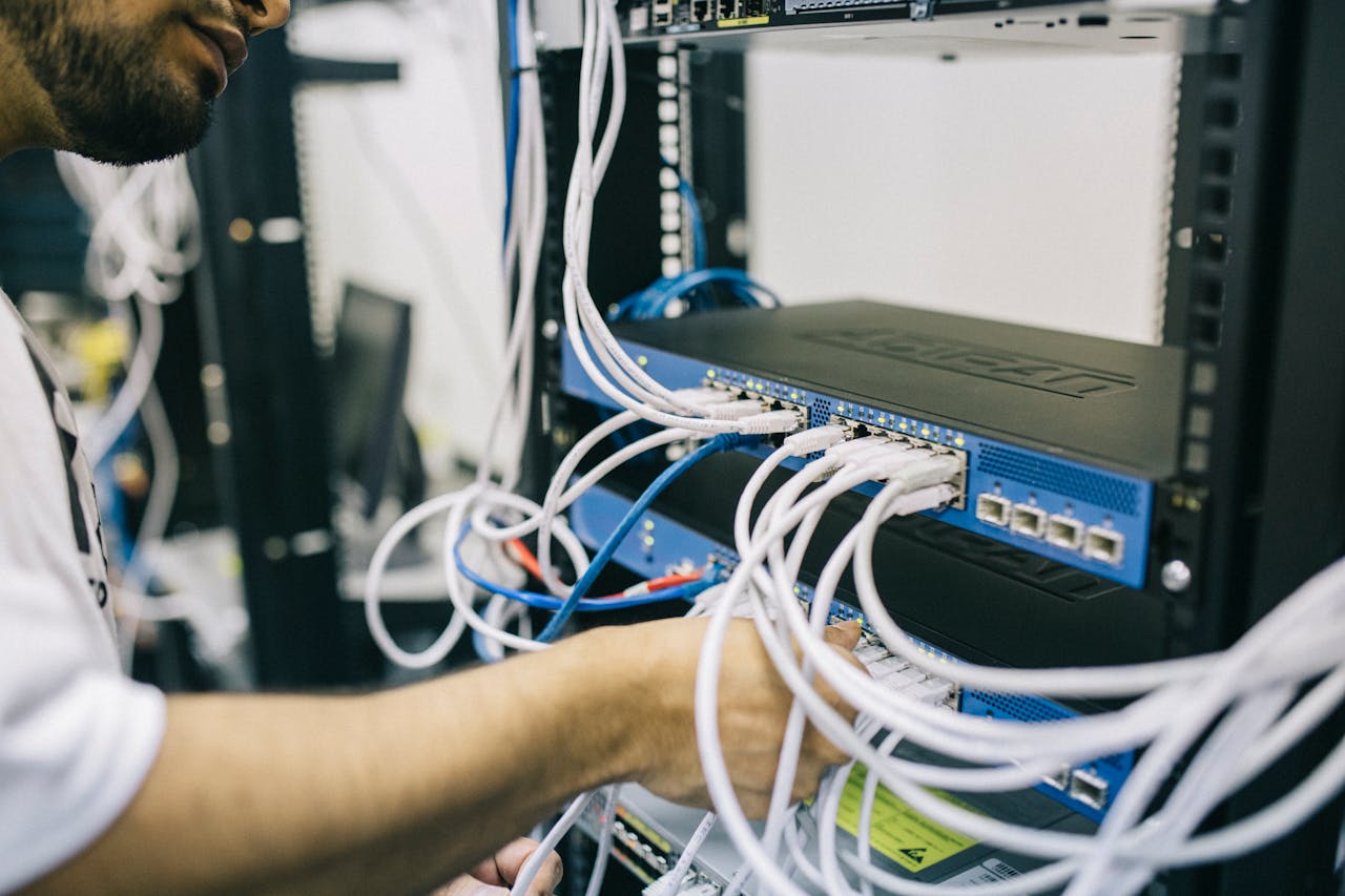 why-choose-us-03 An IT professional configuring network cables in a server rack, focusing on Ethernet connections.